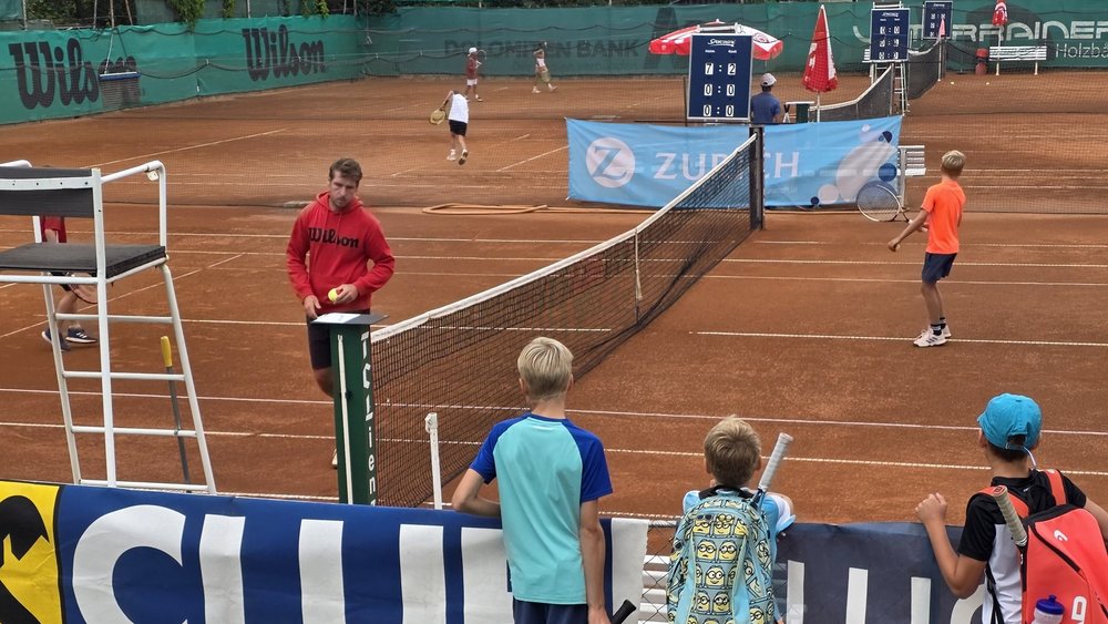 Tennisspieler mit Ball und Schiedsrichterstuhl auf Sandplatz in Österreich